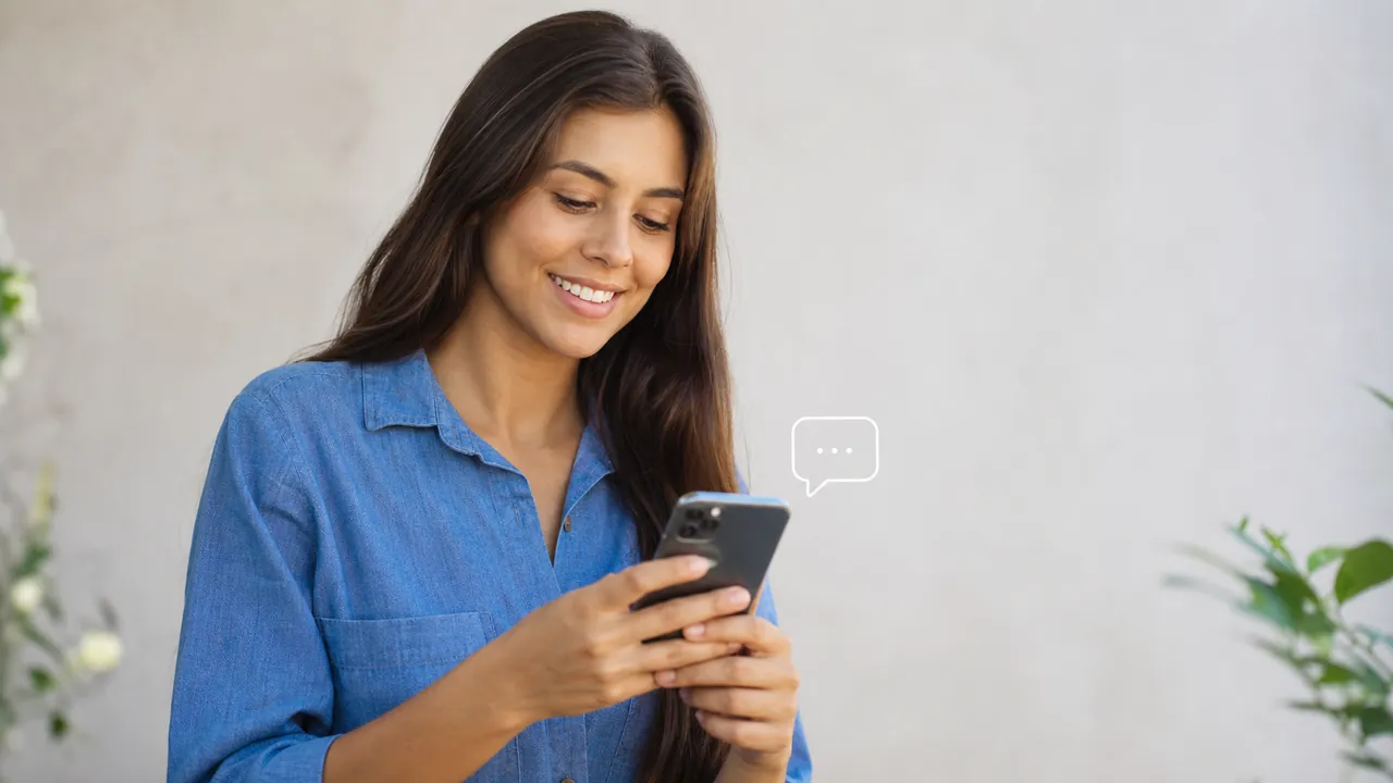 Pessoa sorrindo enquanto responde mensagens e comentários pelo celular